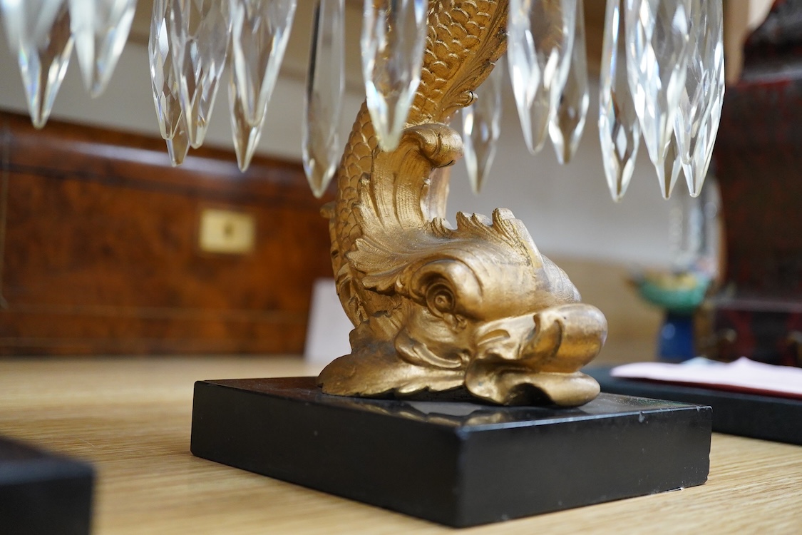 A pair of William IV gilt metal candlesticks, the stems formed as dolphins, with glass lustre drops, raised on square slate bases, 37cm high